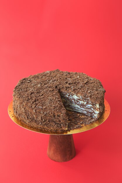 Torta di compleanno a fette sul supporto per torta in legno. Bellissima torta Napoleone al cioccolato. Sfondo rosso. Copia spazio. Fotografia di cibo per ricetta.