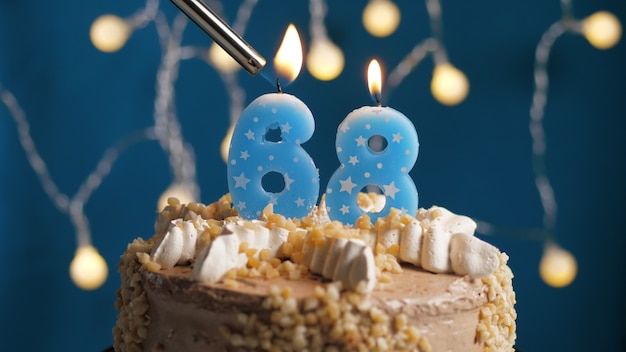 Torta di compleanno con 68 candele numeriche su sfondo blu incendiate da un accendino. Avvicinamento