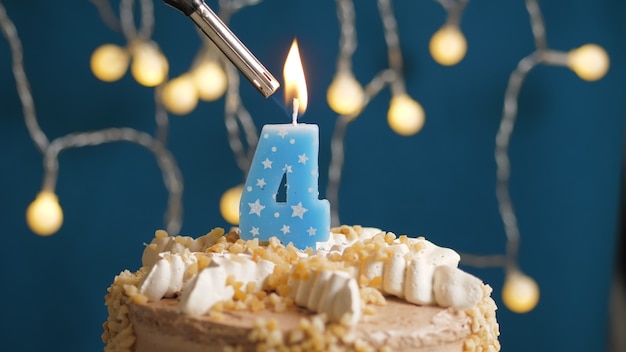 Torta di compleanno con candela a 4 numeri su sfondo blu incendiata da un accendino. Avvicinamento