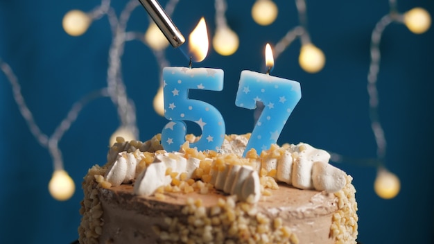 Torta di compleanno con candela numero 57 su sfondo blu incendiata da un accendino. Avvicinamento