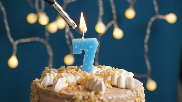 Torta di compleanno con candela numero 7 su sfondo blu incendiata da un accendino. Avvicinamento