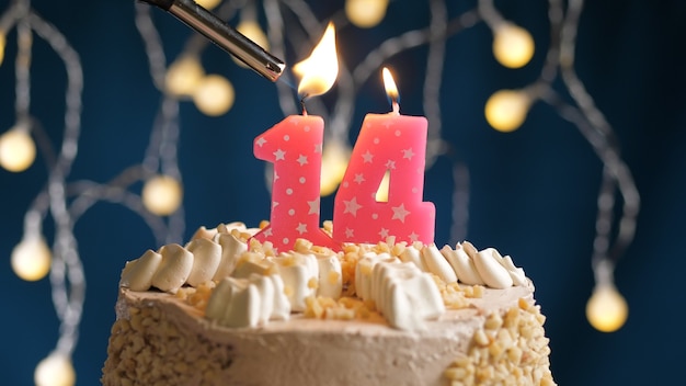 Torta di compleanno con candela rosa di 14 numeri su sfondo blu incendiata da un accendino. Vista ravvicinata