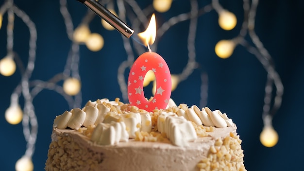 Torta di compleanno con candela rosa numero 0 su sfondo blu incendiata da un accendino. Vista ravvicinata