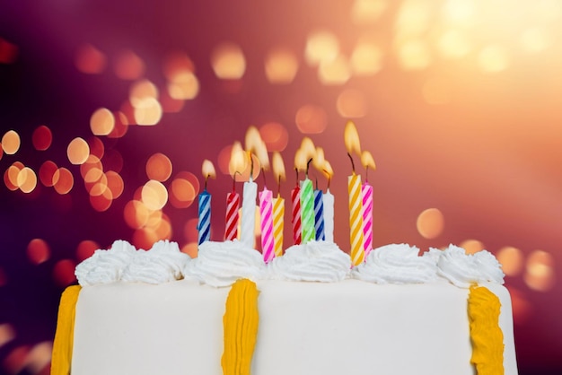 Torta di compleanno con candele colorate nel bagliore delle luci