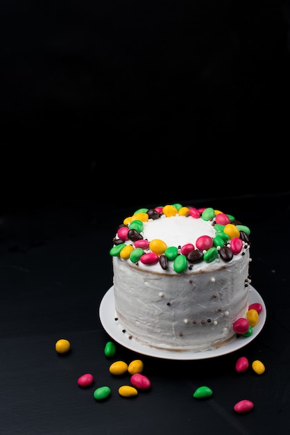 Torta di compleanno con decorazioni in crema e caramelle su una superficie nera