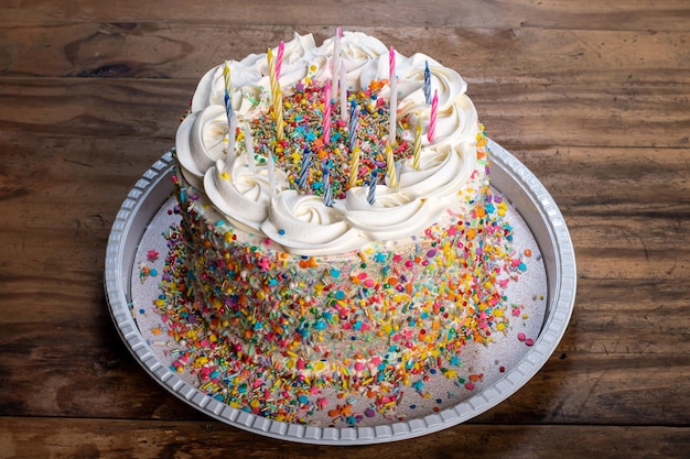 torta di compleanno multicolore con coriandoli, candele sulla torta, fondo in legno
