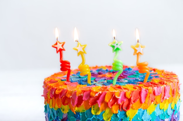 Torta di compleanno multicolore decorata con candele accese a forma di stelle. Buon quarto compleanno concetto.