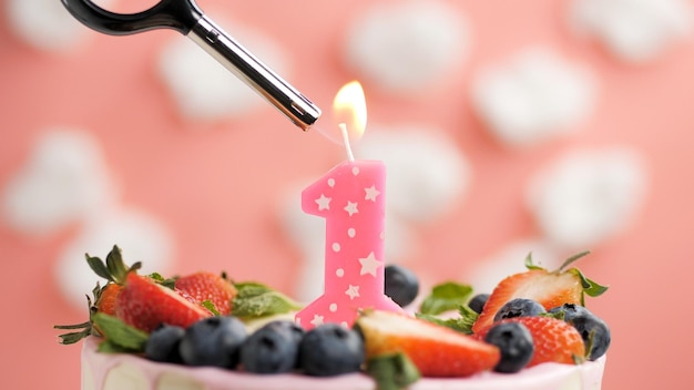 Torta di compleanno numero 1 candela rosa sulla bella torta con frutti di bosco e accendino con fuoco su sfondo di nuvole bianche e cielo rosa Vista ingrandita