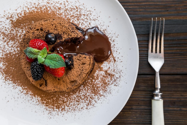 Torta di lava fondente al cioccolato decorata con fragole e polvere di cacao su fondo di legno