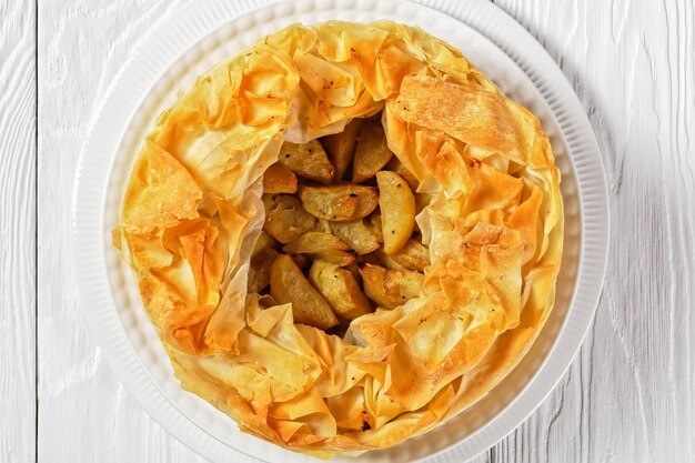 Torta di mele a strati con crosta di Phyllo su un piatto bianco su un tavolo di legno bianco, vista orizzontale dall'alto, piatto, spazio libero