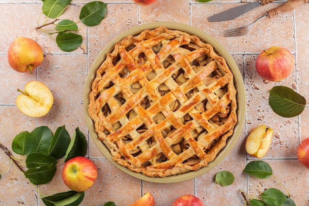 Torta di mele fatta in casa con mela rossa fresca e foglie su piastrelle di travertino beige sullo sfondo del tavolo sopra da vicino