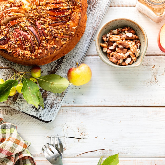 Torta di mele fatta in casa e ingredienti su una superficie di legno bianca