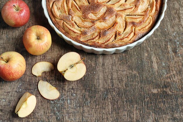 Torta di mele tradizionale francese fatta in casa in una forma di cottura in ceramica bianca e mele sulla tavola di legno