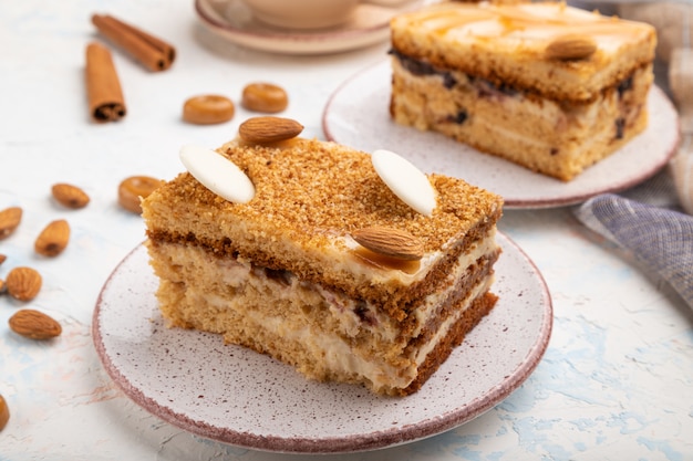 Torta di miele con crema di latte, caramello, mandorle e una tazza di caffè su uno sfondo di cemento bianco. Vista laterale, da vicino.