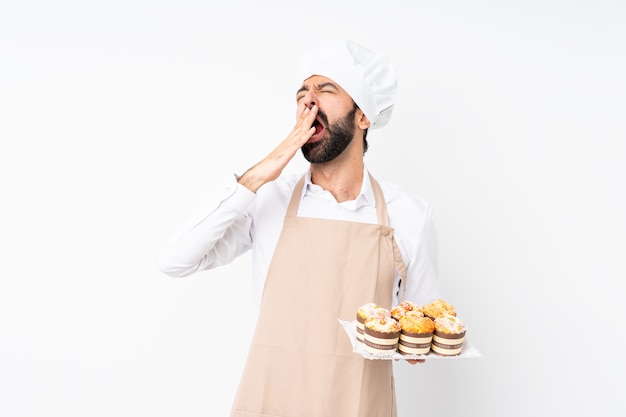 Torta di muffin della tenuta del giovane che sbadiglia e che copre bocca spalancata di mano