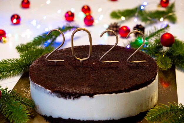 Torta di Natale con candele dorate 2022 numero sopra la torta al cioccolato con luci bokeh sullo sfondo. Buon Natale e Felice Anno nuovo. Preparazione per la celebrazione.