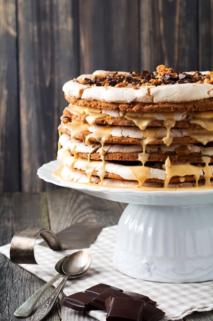 Torta di pasticceria a strati fatta in casa e meringa, noci, cioccolato fondente su legno vecchio