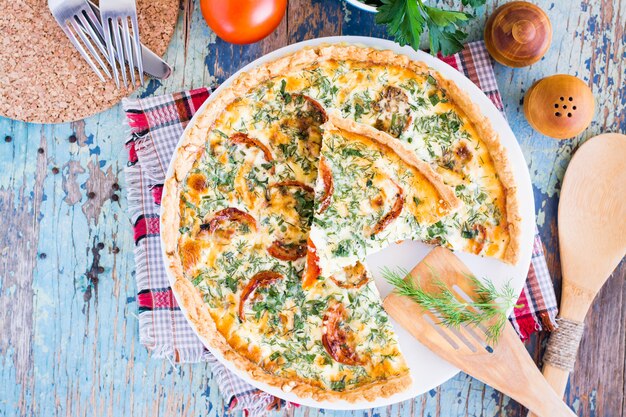 Torta di quiche francese casalinga affettata con il pomodoro, il formaggio e l'erba su un piatto. Vista dall'alto