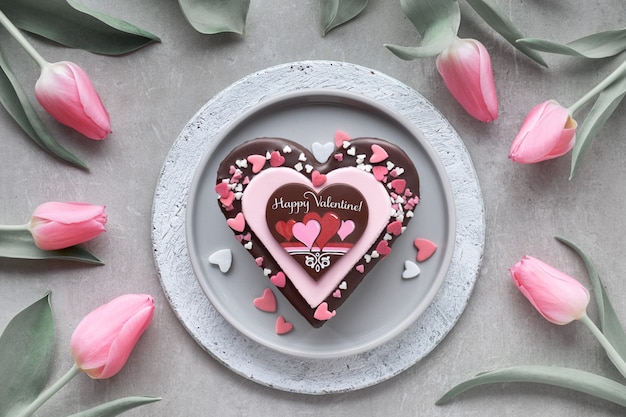 Torta di San Valentino con cioccolato, decorazioni di zucchero e testo "Happy Valeitine" e un mazzo di tulipani rosa