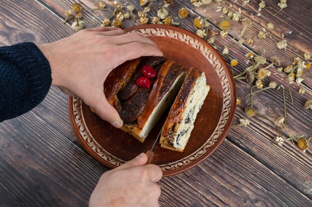 Torta di taglio a mano maschio con semi di papavero posto su un tavolo di legno.