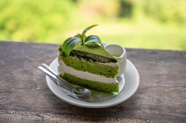 Torta di tè verde biologico a fette con panna montata e foglia di tè in piatto bianco su barra di legno in piantagione