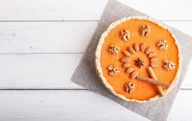 Torta di zucca dolce americana tradizionale decorata con le noci, su superficie di legno bianca.