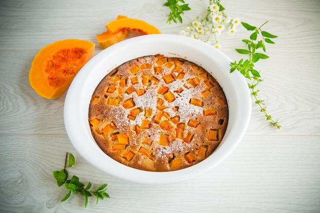 Torta di zucca dolce con fette di zucca in uno stampo in ceramica su un tavolo di legno