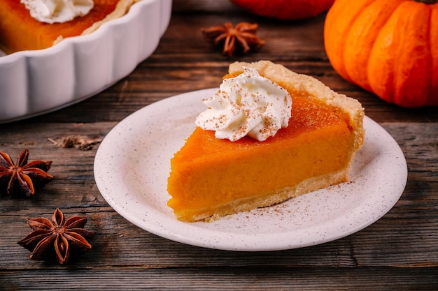 Torta di zucca fatta in casa per il Ringraziamento con panna montata e cannella su fondo di legno