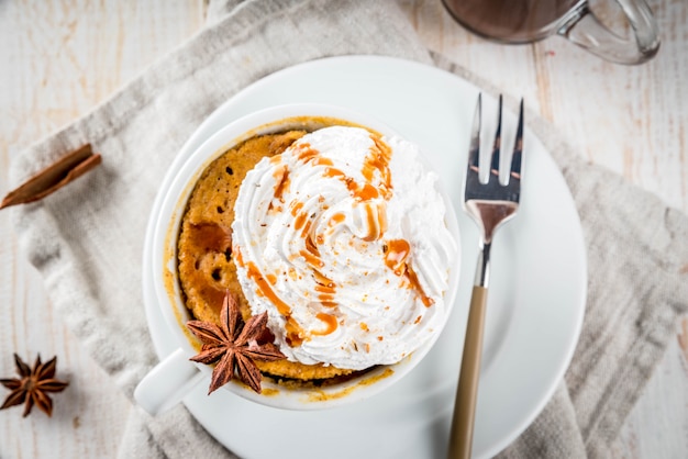 Torta di zucca piccante in tazza, con panna montata, gelato, cannella, anice. Sul tavolo di legno bianco, con una tazza di cioccolata calda.