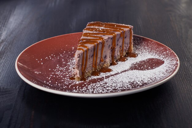 Torta dolce da dessert su un piatto, bella porzione, superficie scura.