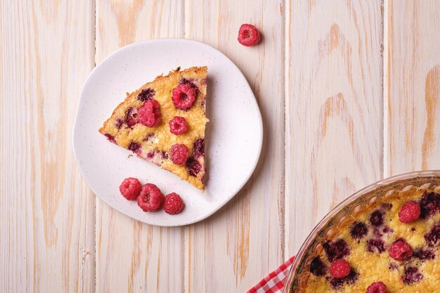 Torta dolce gustosa con lamponi gelatinosi e freschi in teglia e piastra con tovaglia rossa, tavolo in legno, vista dall'alto