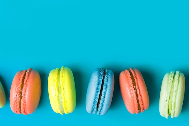 Torta dolce macaron o amaretto su sfondo blu con copia spazio, colori pastello, vista dall'alto. Giallo, corallo, pasticceria francese verde, colazione