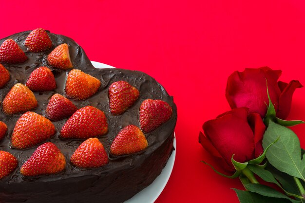 Torta e rose rosse a forma di cuore per il San Valentino o la festa della mamma su fondo rosso