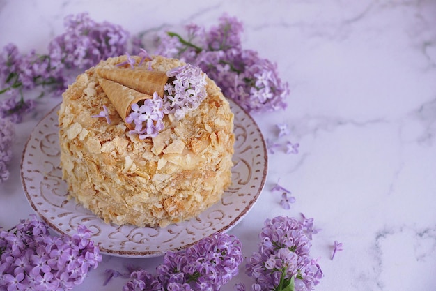 Torta fatta a mano, Napoleone, Millefoglie, Torta a fette di panna su fondo marmoreo con fiori lilla, Pasticceria, Messa a fuoco selettiva