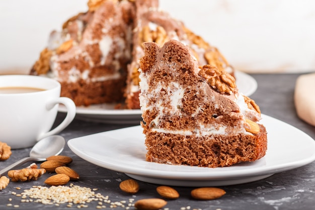 Torta fatta in casa con crema di latte, cacao, mandorle, nocciole su uno sfondo di cemento nero e una tazza di caffè. Vista laterale.