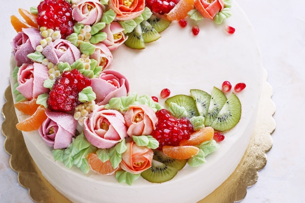 Torta festiva con crema di fiori e frutti su una superficie leggera