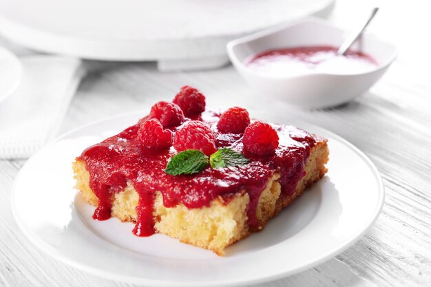 Torta fresca con marmellata di lamponi in piattino bianco sul primo piano della tavola di legno