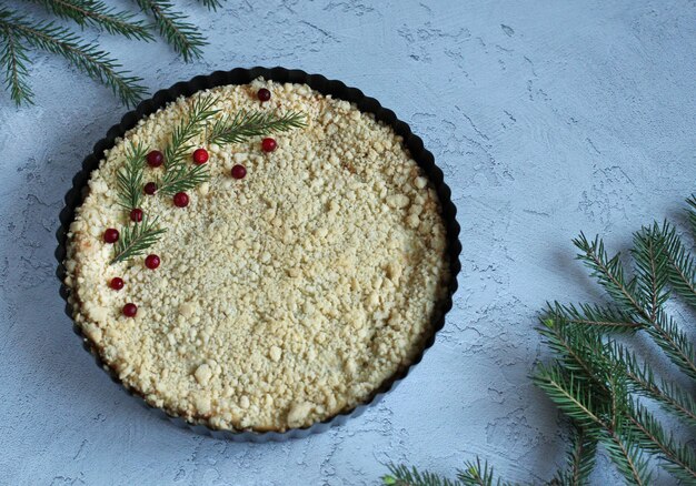 Torta friabile di ricotta in forma nera su uno sfondo grigioblu con rami di abete rosso