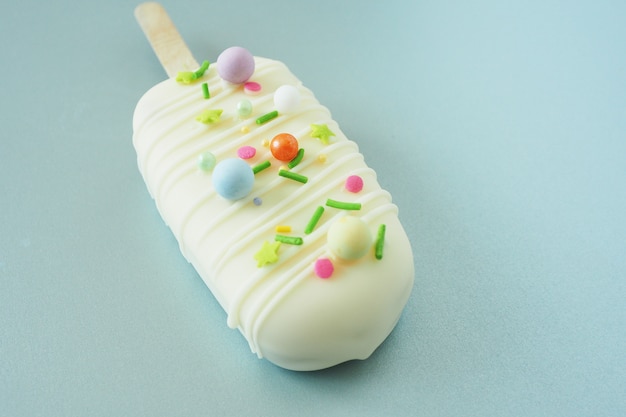 Torta - ghiacciolo in glassa di cioccolato bianco e granelli colorati su fondo argento. spazio per il testo.