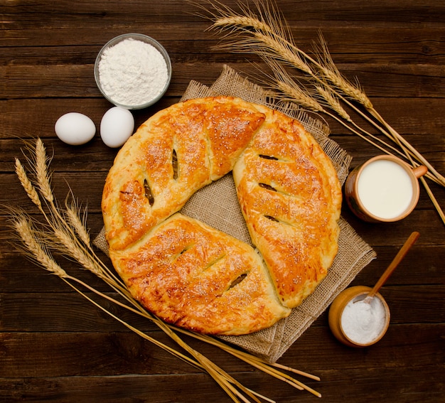 Torta, ingredienti per la cottura, spighe di grano e tazza di latte. Vista dall'alto