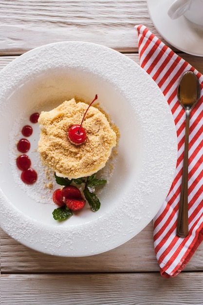 Torta Napoleone su piatto bianco con decorazione di fragola ciliegia e menta Dessert dolce che serve nel ristorante su tavola di legno vista ravvicinata dall'alto