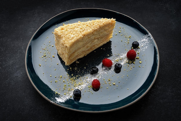 Torta Napoleone su un piatto scuro con frutti di bosco su cemento scuro