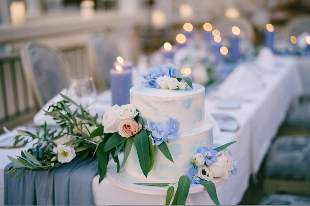 Torta nuziale a castello bianca decorata con fiori e foglie si erge su un tavolo con candele