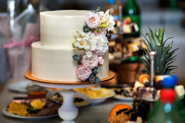 Torta nuziale dolce alta decorata con fiori rosa e bianchi vivi su un tavolo