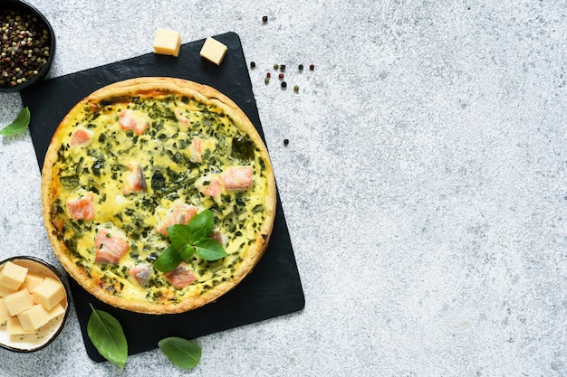 Torta (quiche) con salmone, spinaci e formaggio su una tavola di pietra su un calcestruzzo.