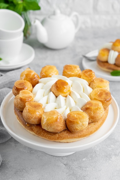 Torta Saint Honore con crema pasticcera al caramello profitrols e panna montata su un piatto bianco