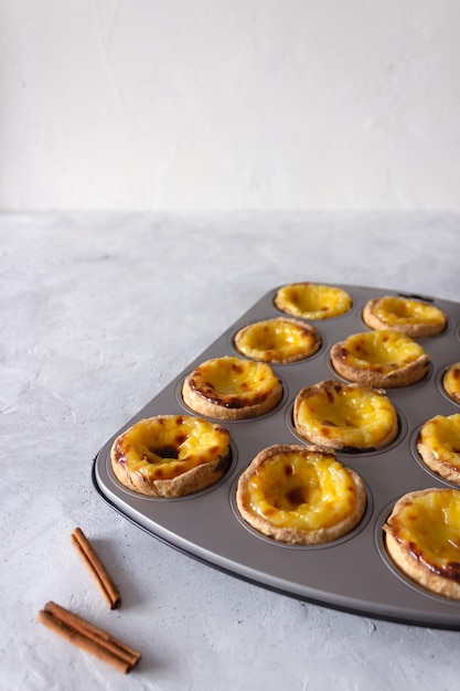 Torte alla crema portoghese pastel de nata nello stampo da forno grigio con bastoncini di cannella