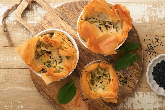 Torte di filo con formaggio feta morbido e spinaci in stampi di ceramica su sfondo di tavolo in legno vecchio Torte di porzioni di filo Piccole torte di Spanakopita al forno Vista dall'alto Copia spazio Cucina greca tradizionale