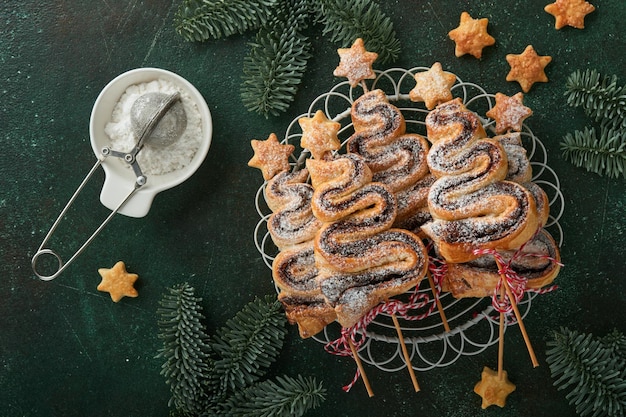 Torte di pasta sfoglia a forma di albero di Natale con ripieno di cioccolato zucchero in polvere e lecca-lecca su vecchio sfondo verde Antipasto di Natale Capodanno Idea festiva per la cena di Natale o Capodanno