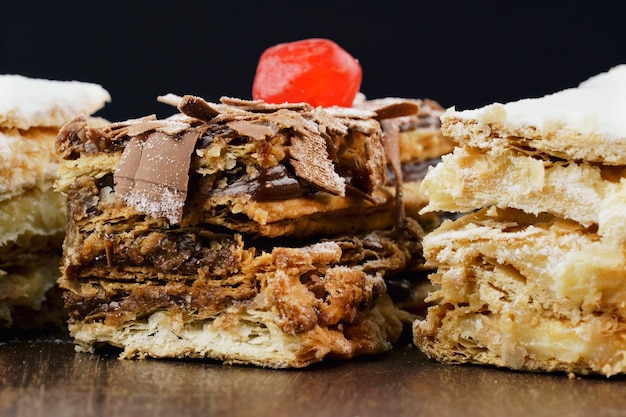 Torte di pasta sfoglia con zucchero a velo e panna e un altro con cioccolato e una ciliegina sulla tavola di legno. Avvicinamento. Messa a fuoco selettiva.